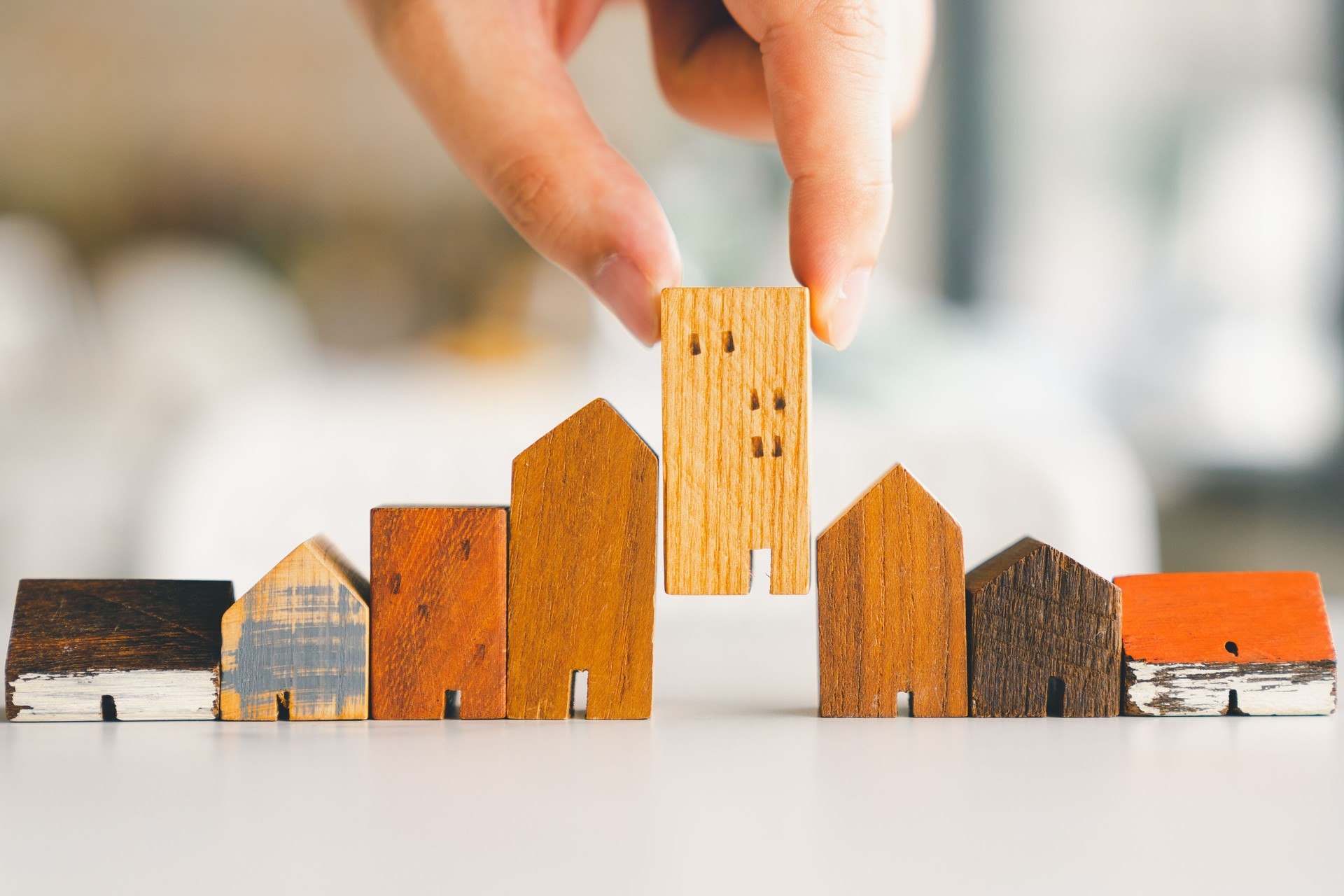 Hand choosing mini wood house model from model and row of coin money on wood table, selective focus, Planning to buy property. Choose what's the best. A symbol for construction ,ecology, loan concepts